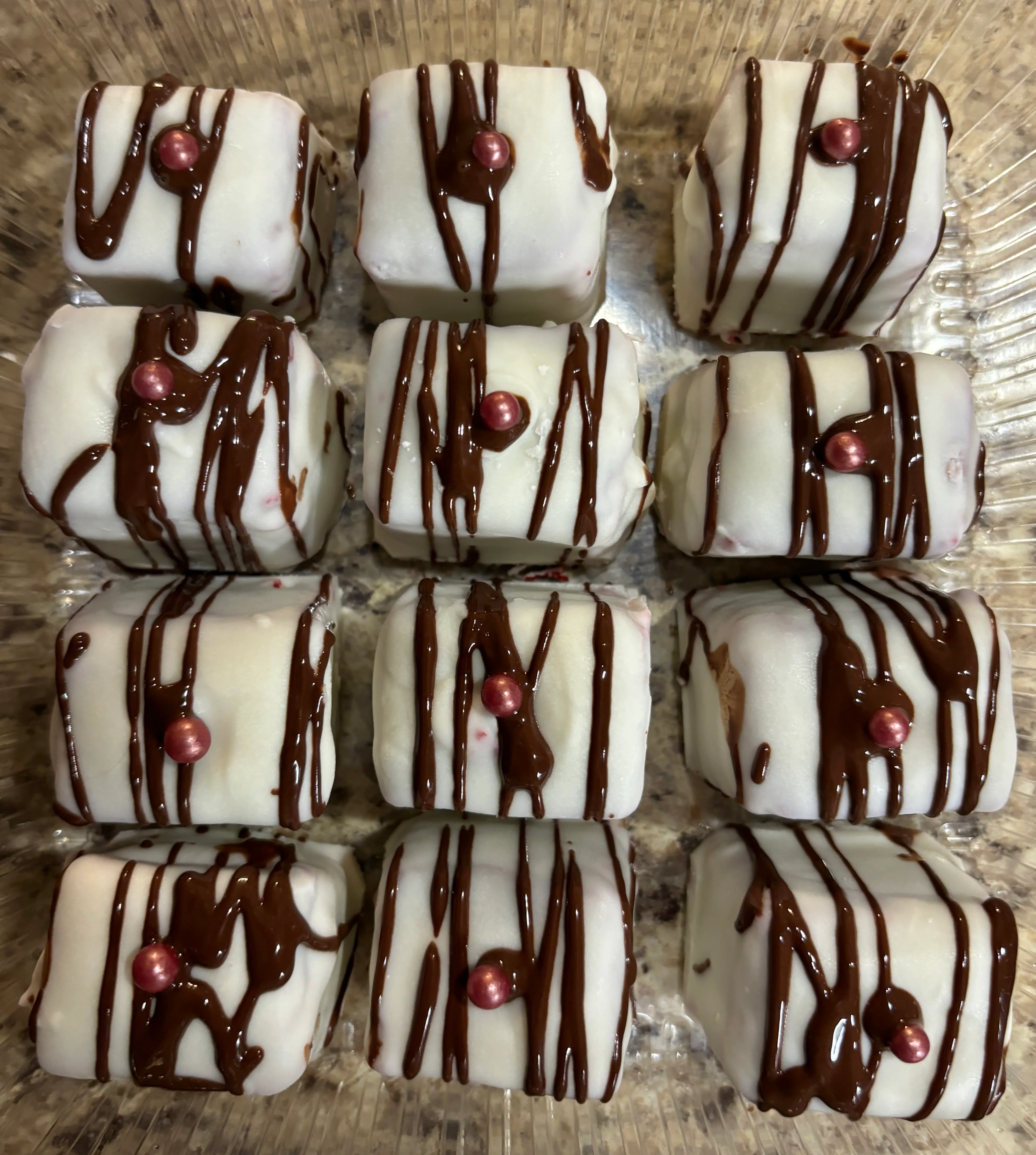 Elegant petit fours with chocolate drizzle and decorative pearls
