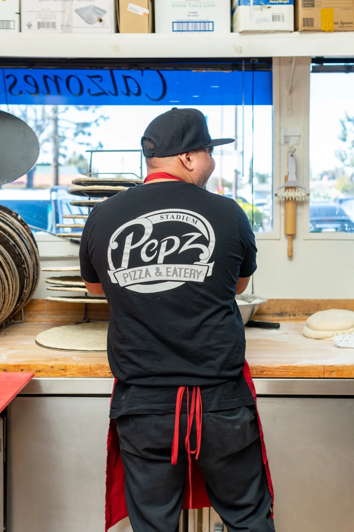 Stadium Pepz cook stretching pizza dough by hand at the make line
