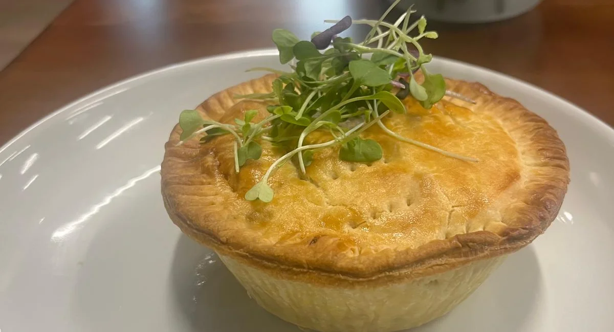 A golden-brown pie topped with microgreens on a white plate.