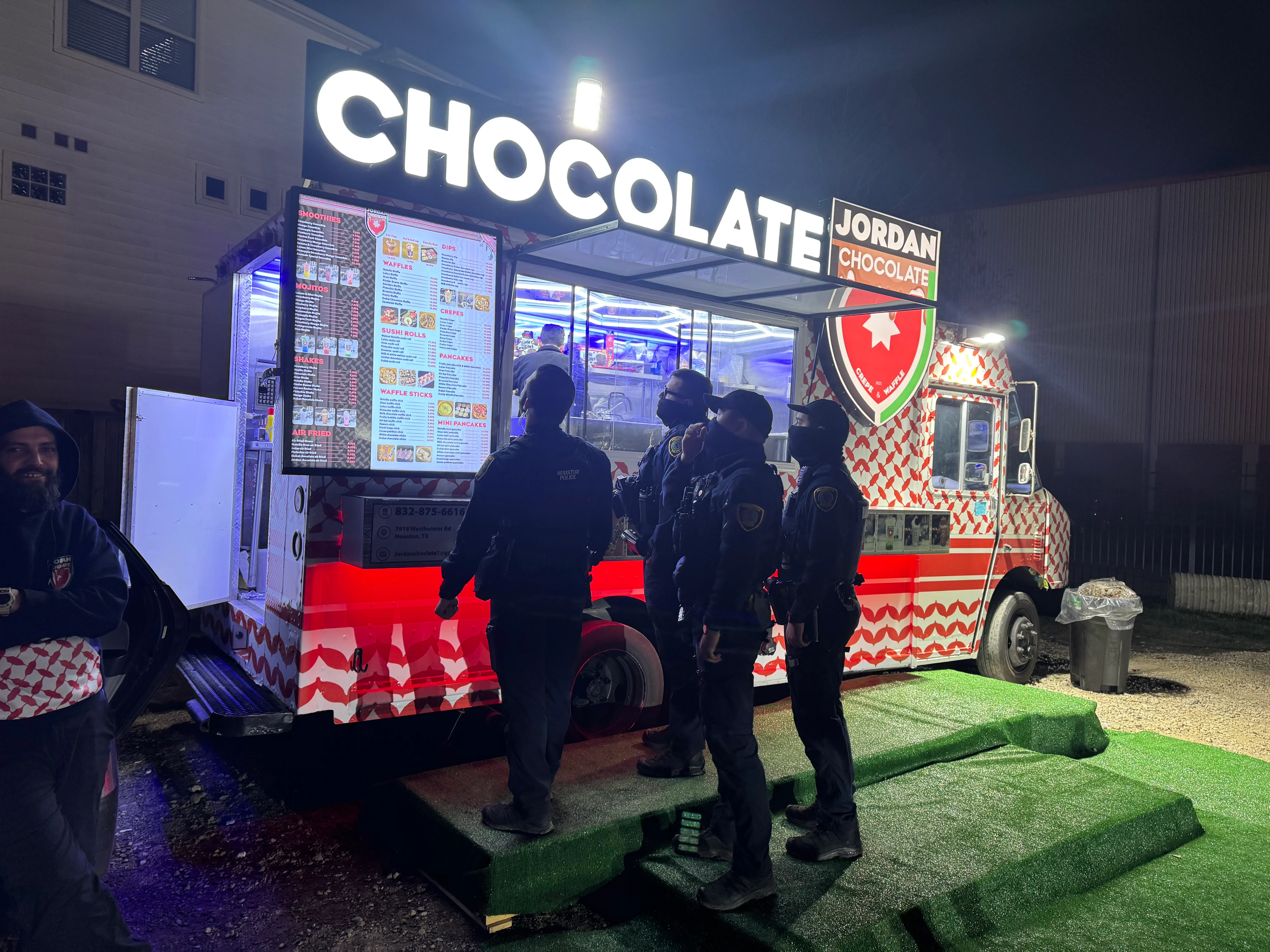 A food truck with a vibrant 'Chocolate' sign and a menu display, surrounded by people at night.