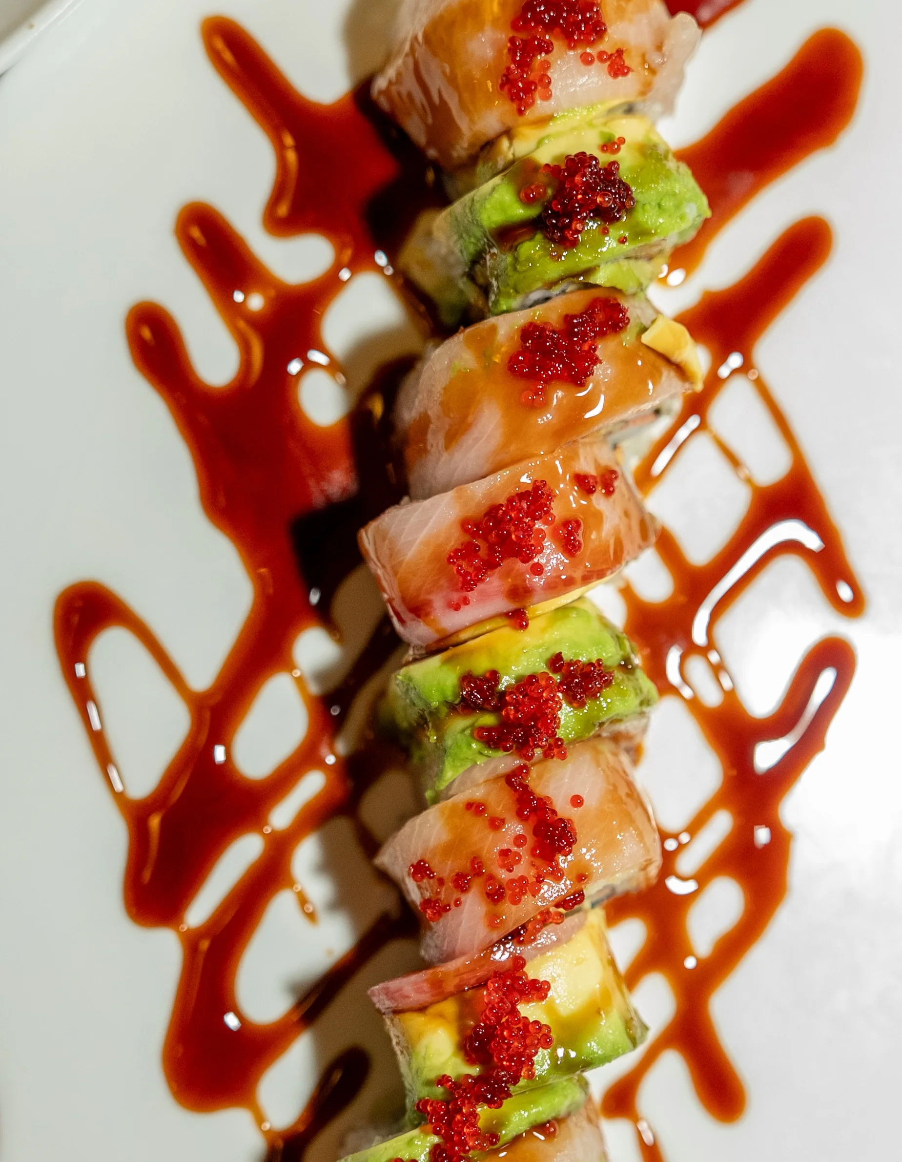 Japanese sushi roll drizzled with sauce and topped with fish roe