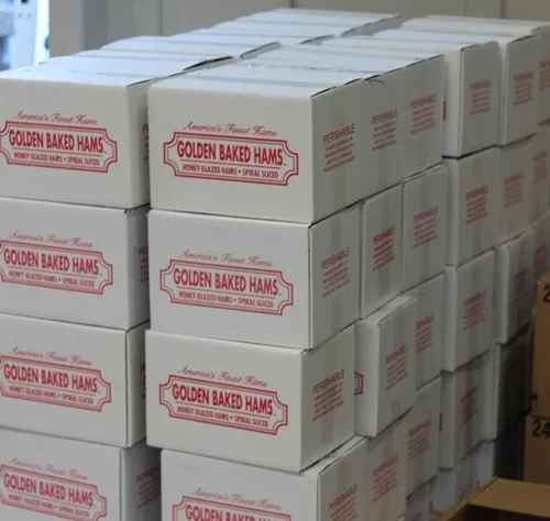 Stacked white boxes labeled Golden Baked Hams in a restaurant storage area