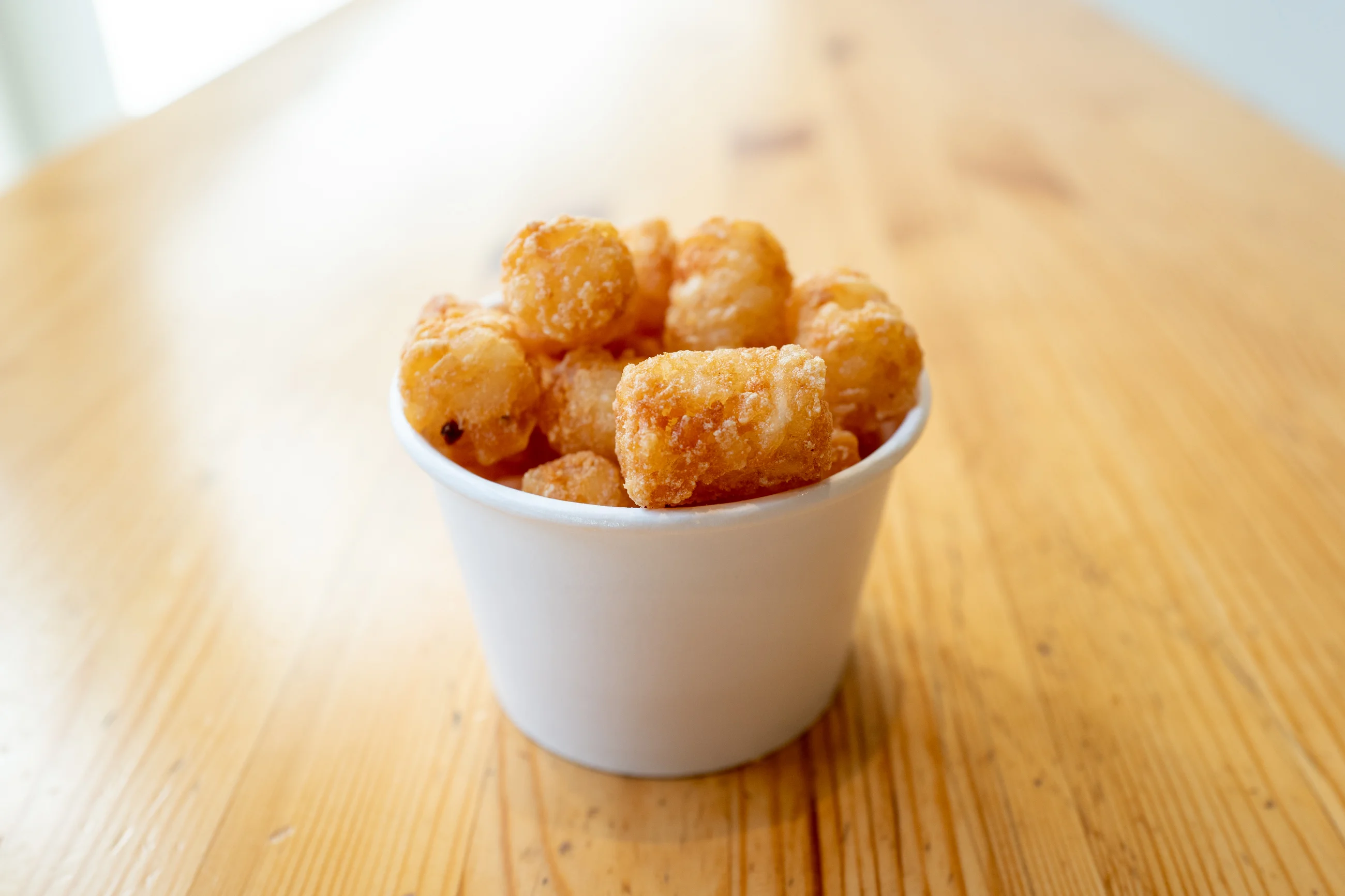 A cup filled with crunchy, golden-brown tater tots, placed on a wooden table.