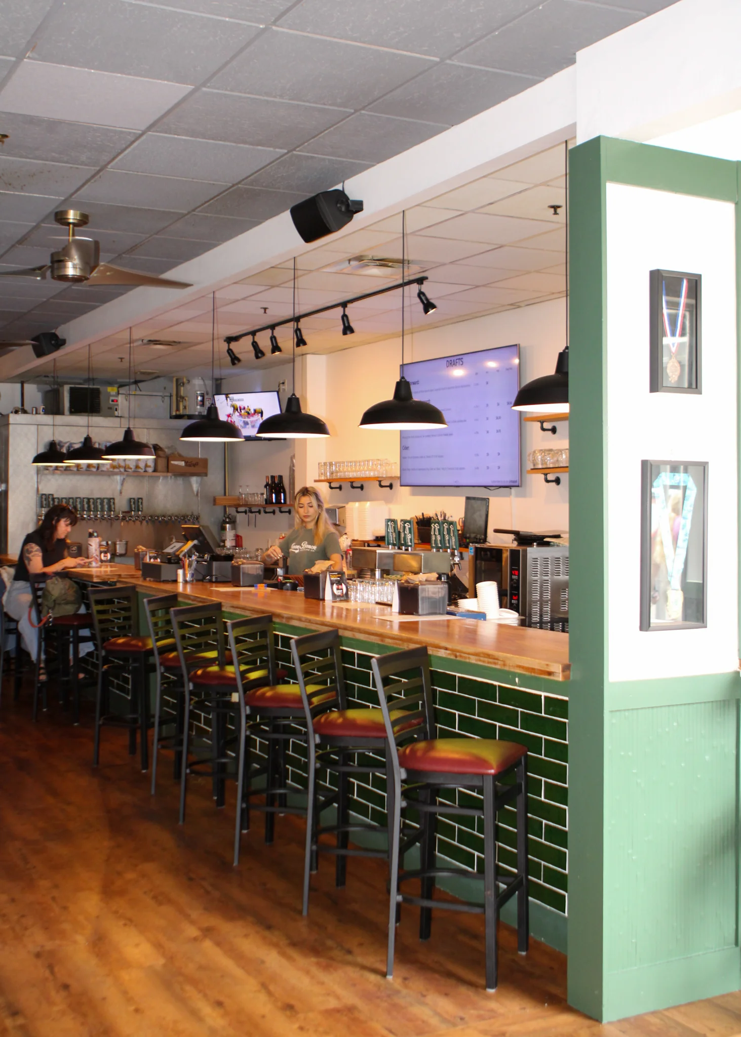 An interior view of a bar area, featuring a long countertop with seating and a display of drinks and a menu board.