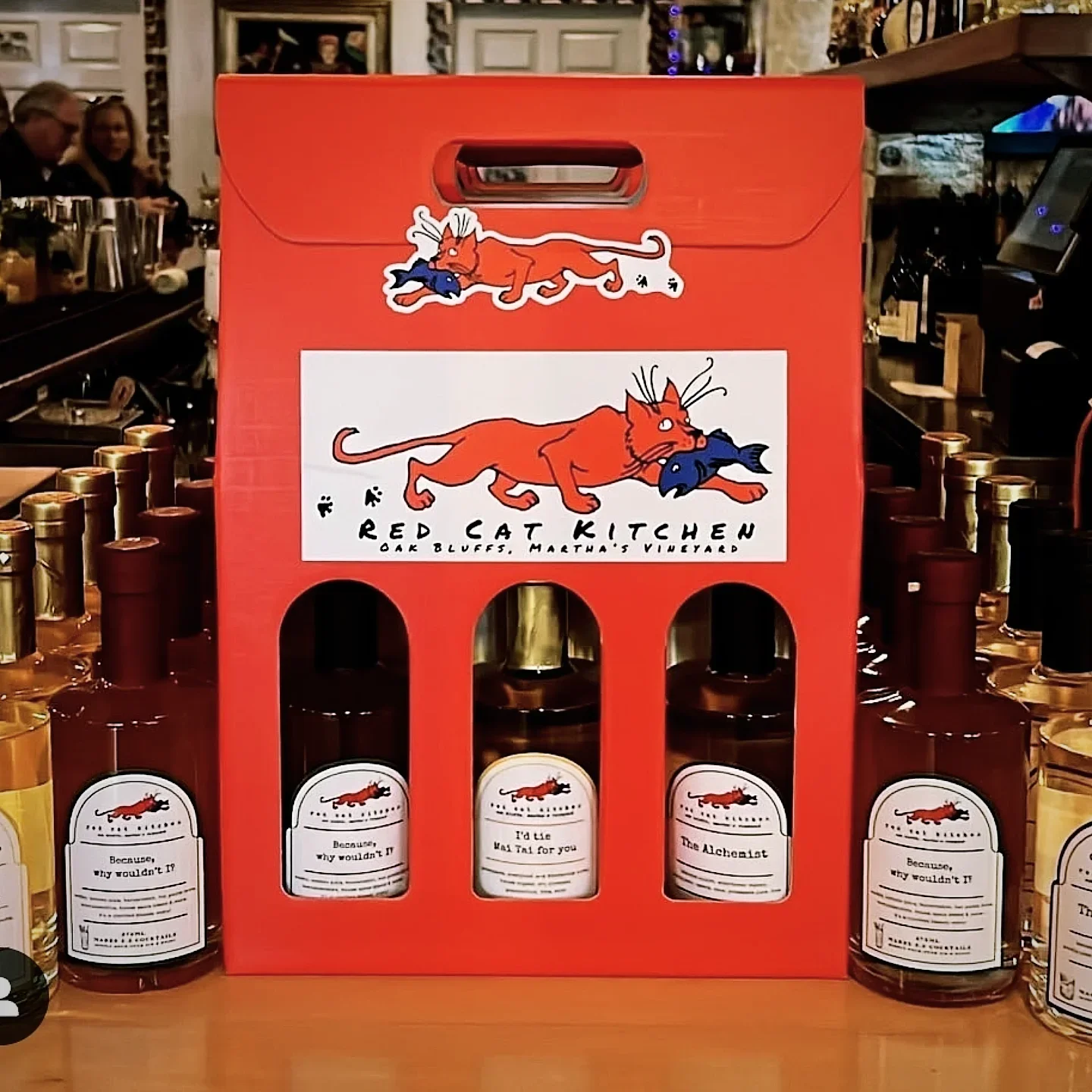 A red carry pack featuring bottles labeled with playful designs, showcasing a local kitchen brand.