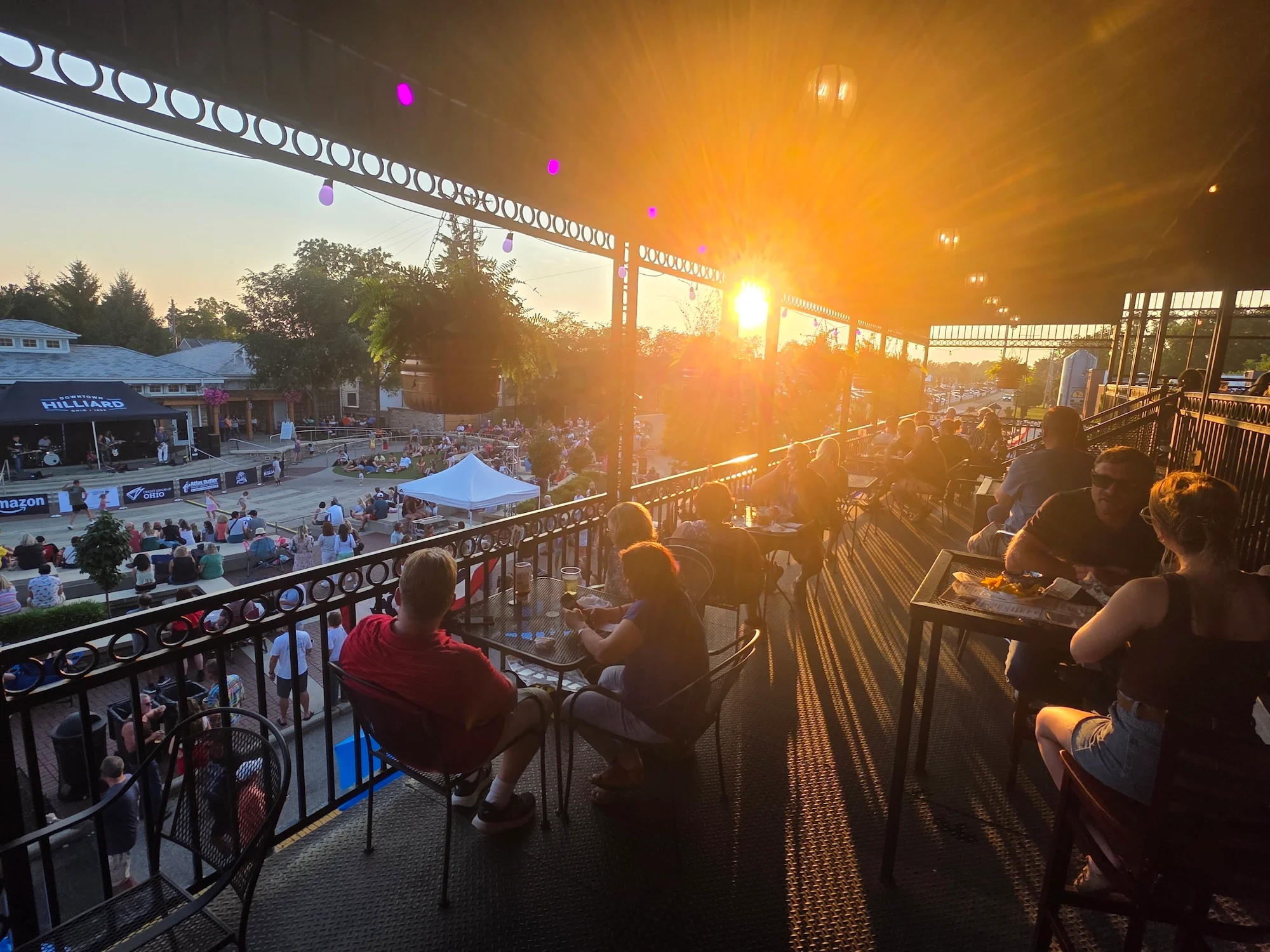 A sunset view from an upper balcony overlooking a lively outdoor event with seated guests enjoying the atmosphere.