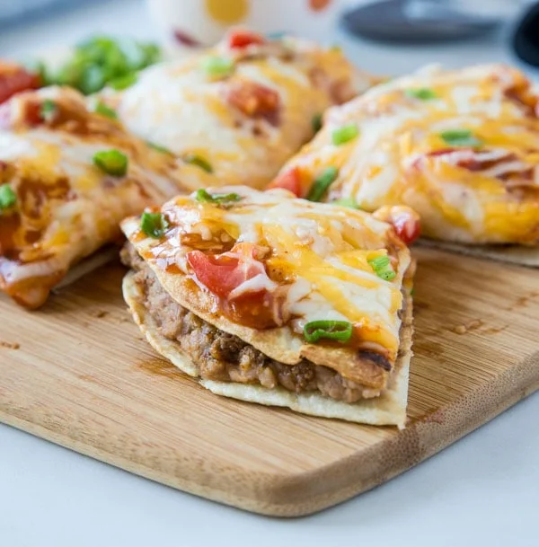 A serving of cheesy tortillas topped with beans, tomatoes, and green onions on a wooden board.