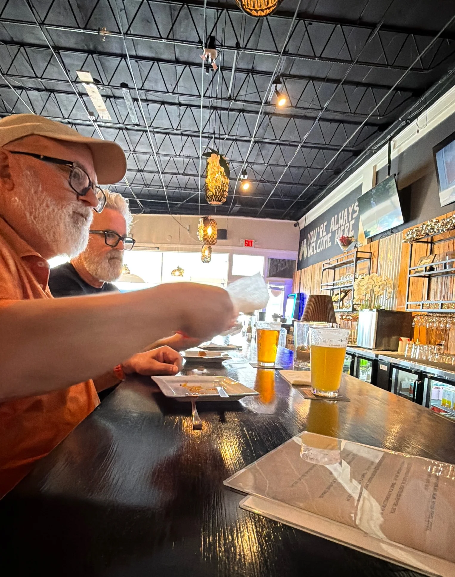 A casual dining scene at a bar, with patrons engaged in conversation and drinks on the table.