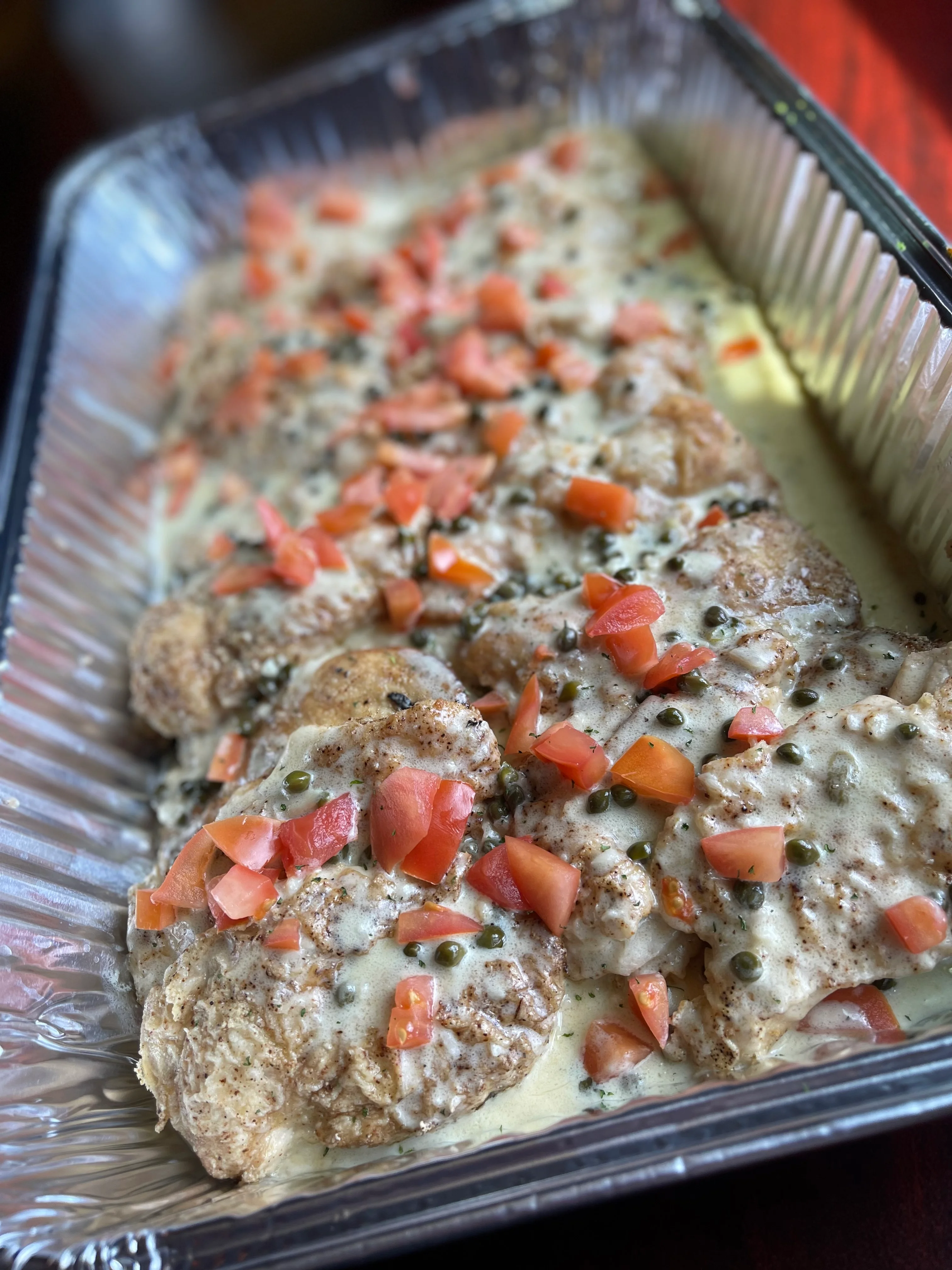 Baked chicken piccata with melted cheese and fresh tomatoes