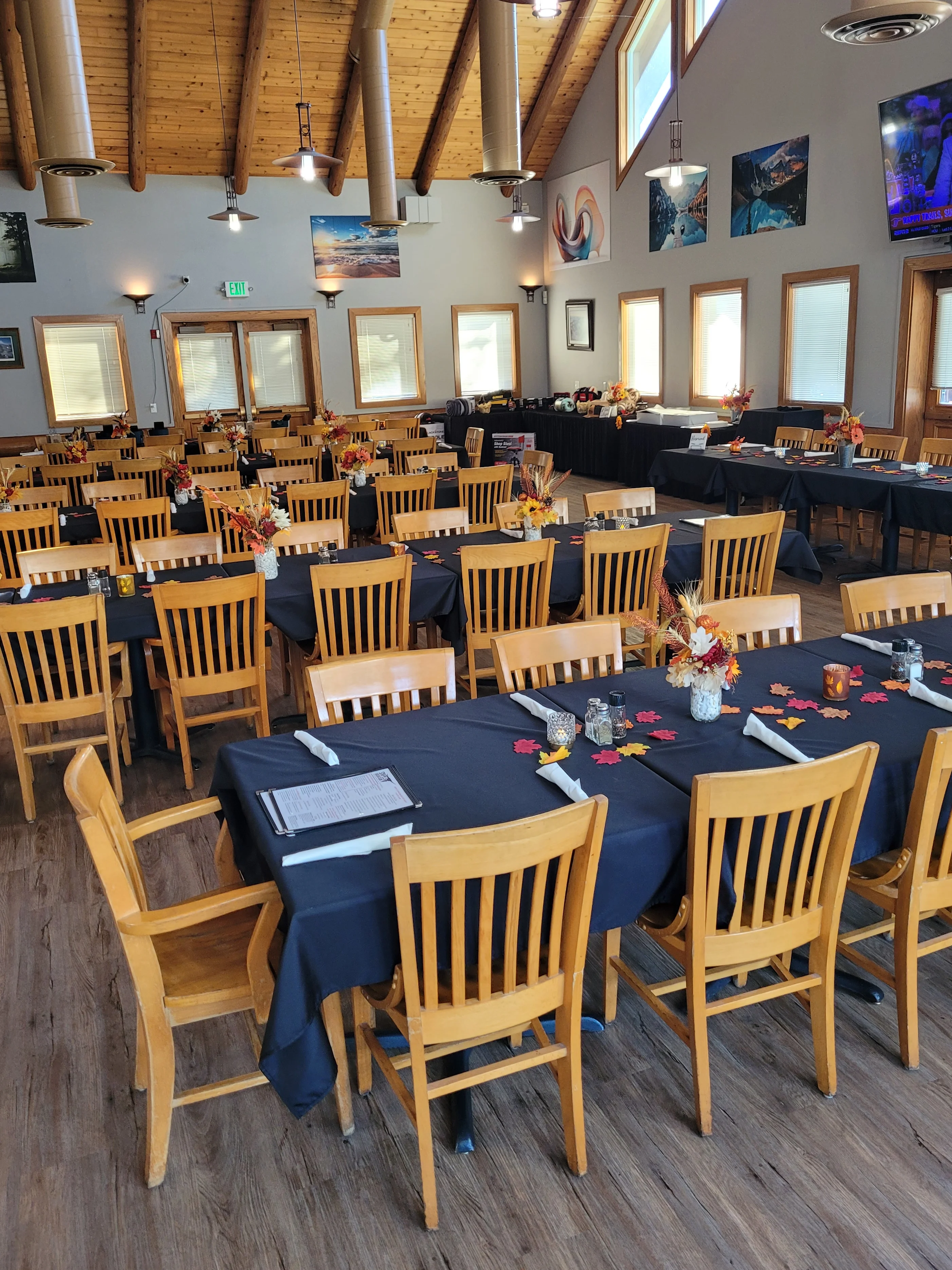 A spacious dining area featuring wooden furniture, booths, and large windows allowing natural light to fill the space. The design includes rustic elements like stone and wood.
