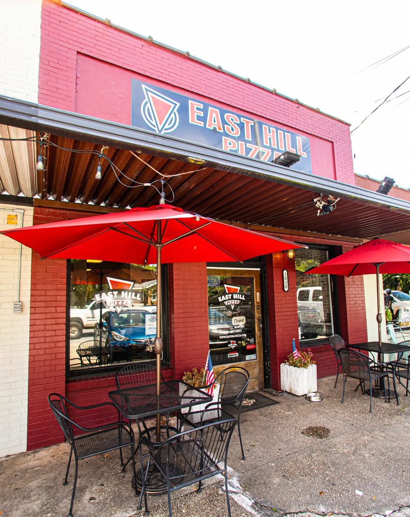 East Hill Pizza restaurant exterior with red umbrellas and outdoor seating