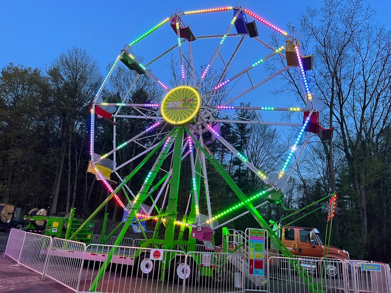 A brightly lit ferris wheel at dusk, showcasing vibrant colors against a backdrop of trees.