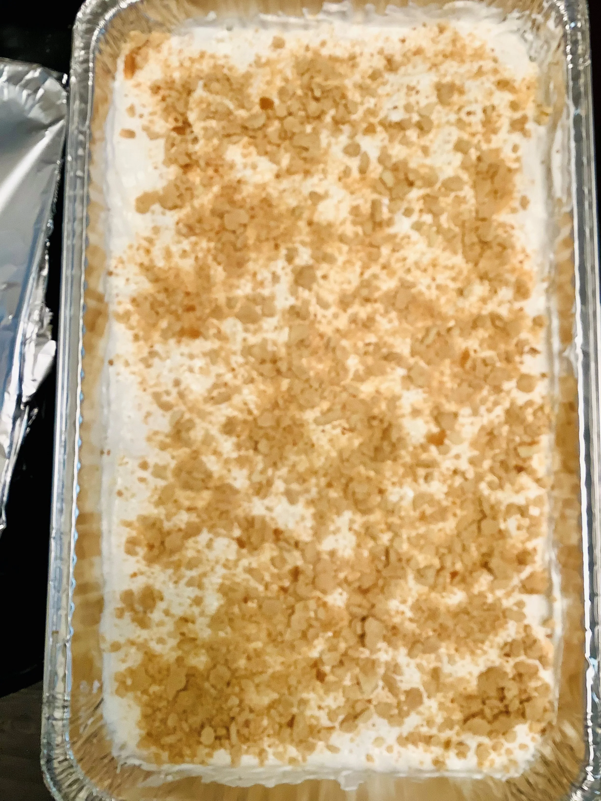 A rectangular dish filled with a creamy dessert topped with crushed cookies. The surface is mostly white with scattered crumbs.