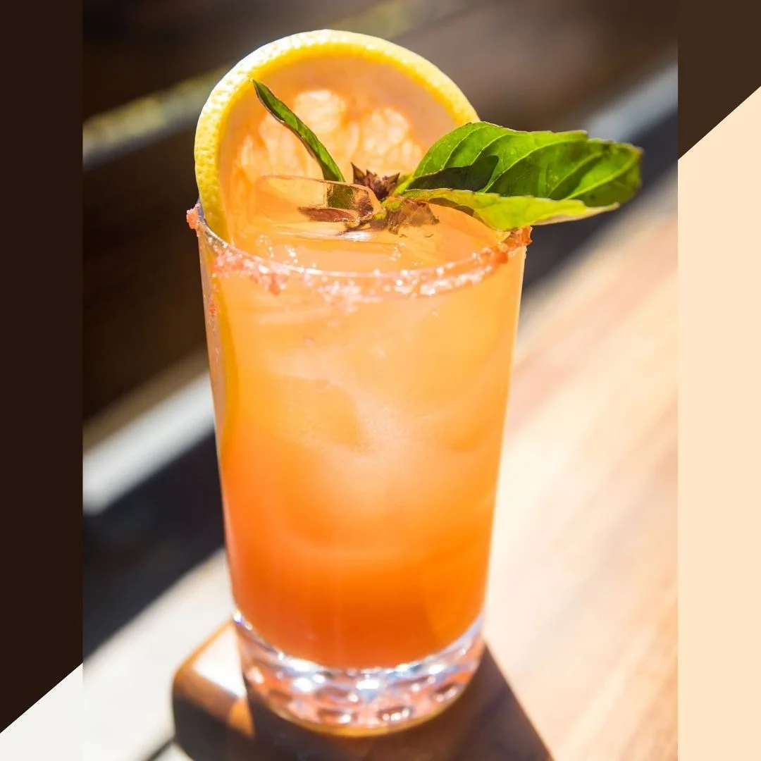A refreshing cocktail garnished with a lemon slice and a basil leaf, presented in a clear glass with a sugared rim.