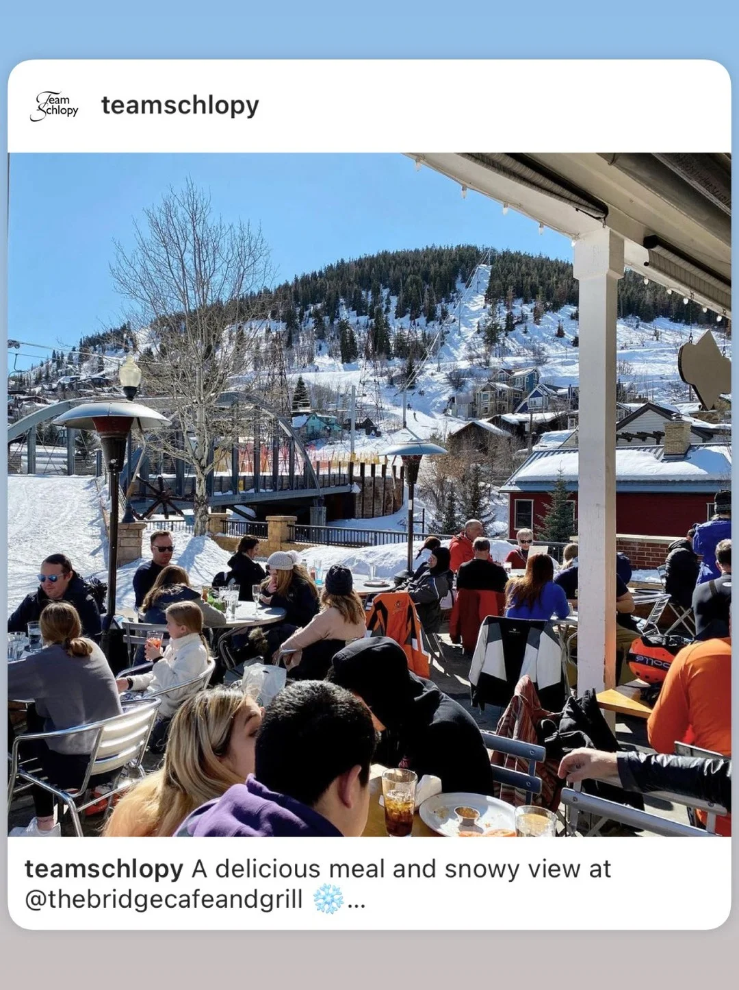 An outdoor dining area with patrons enjoying meals and a snowy mountain view in the background.