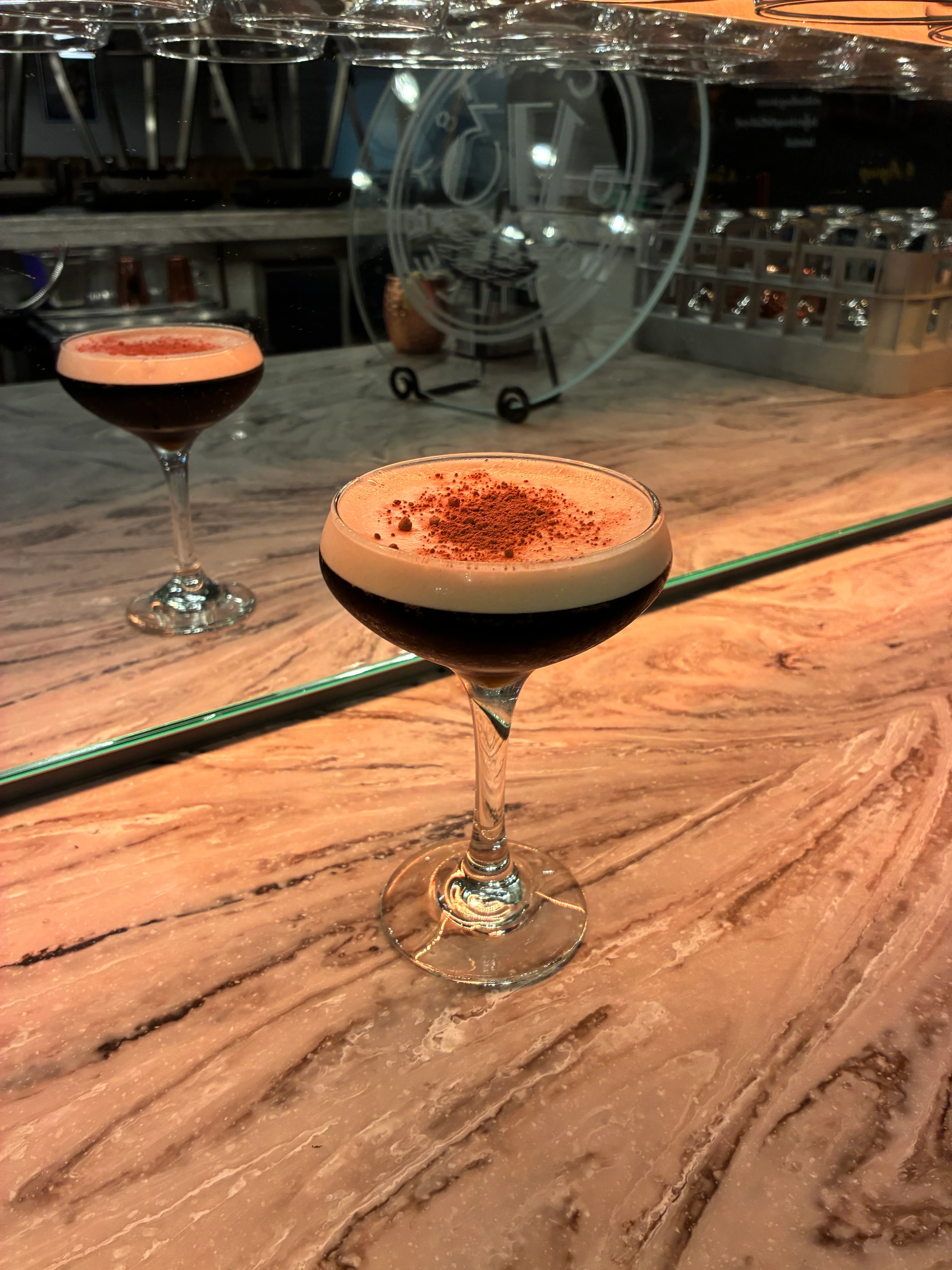 A close-up view of a red cocktail in a glass on a wooden surface, featuring a few ice cubes and a garnish of berries.