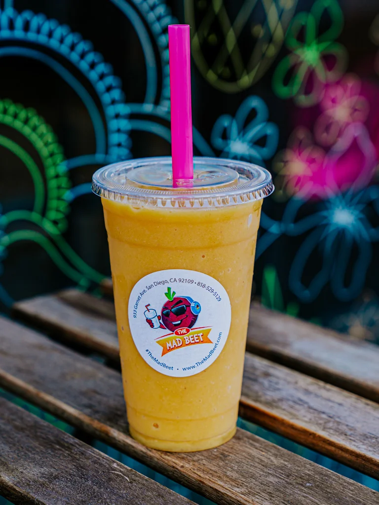 Fresh Florida Georgia Lime smoothie sitting on a wooden table, in a disposable cup featuring The Mad Beet logo