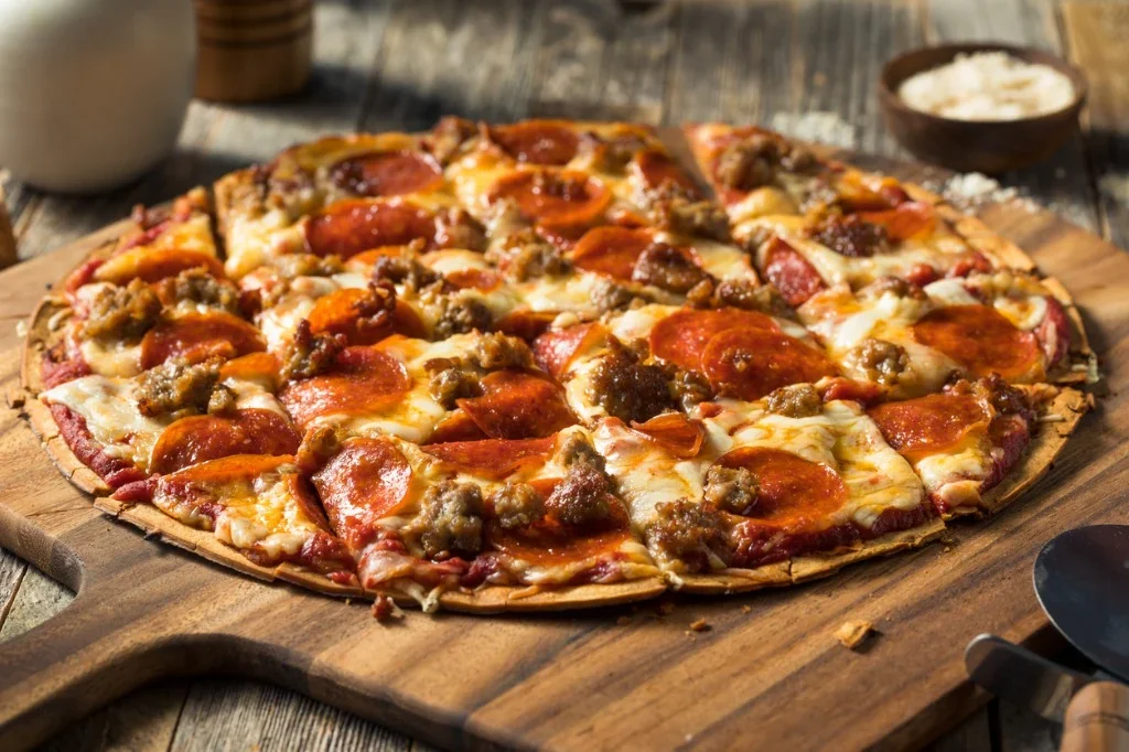 A freshly baked pizza topped with pepperoni and sausage on a wooden serving board.