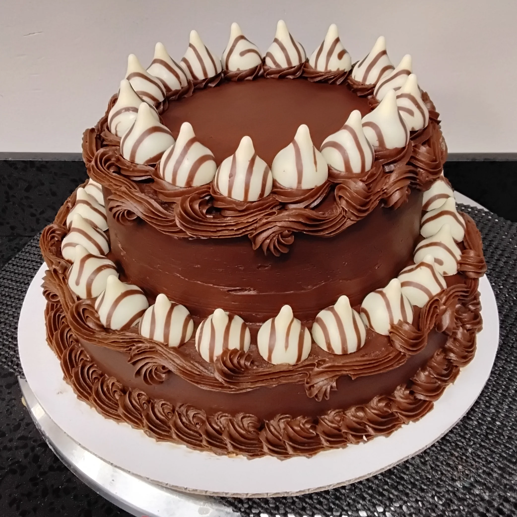Round two layered cake with chocolate frosting and Hershey kisses edging each layer.