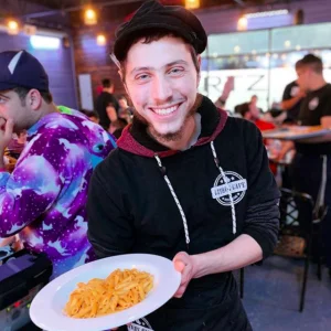 Smiling server presenting a plate of pasta in a lively restaurant