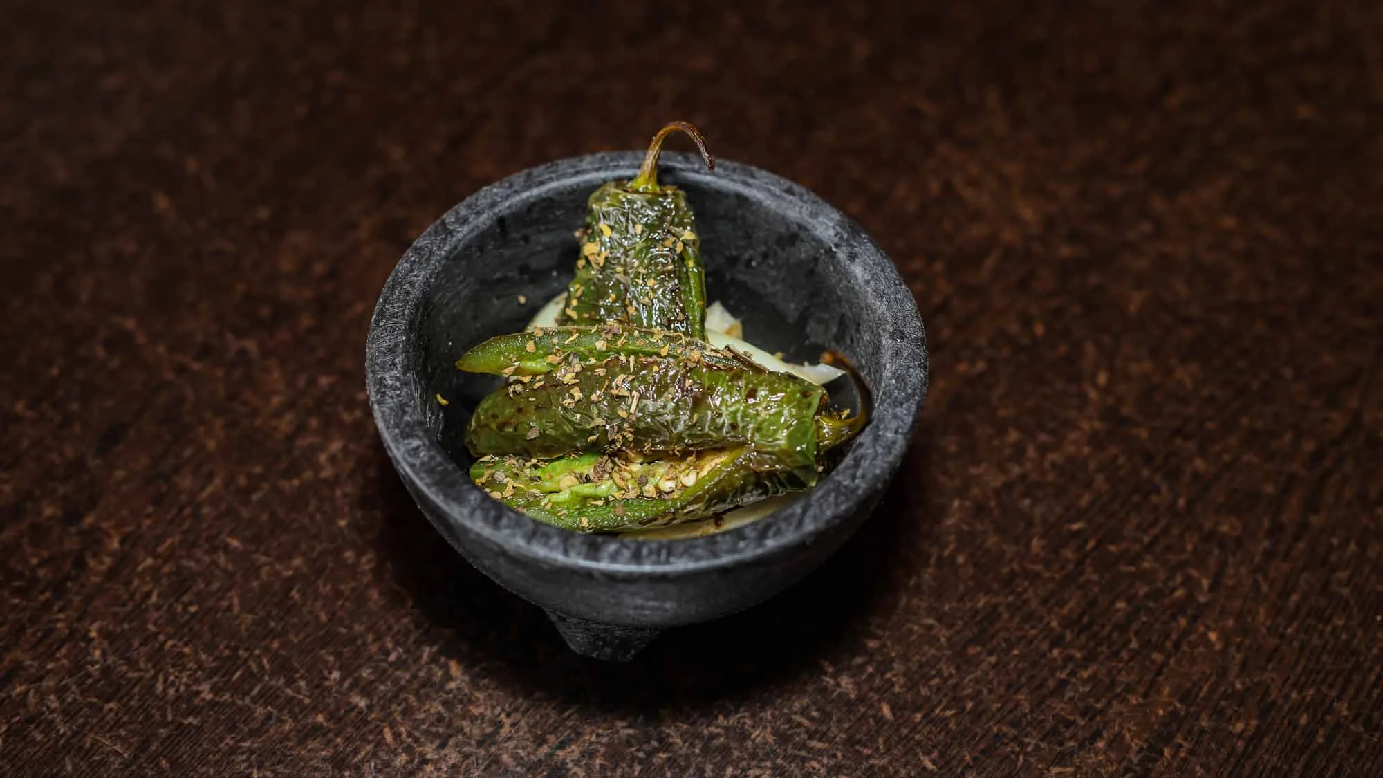 Grilled shishito peppers in a stone bowl