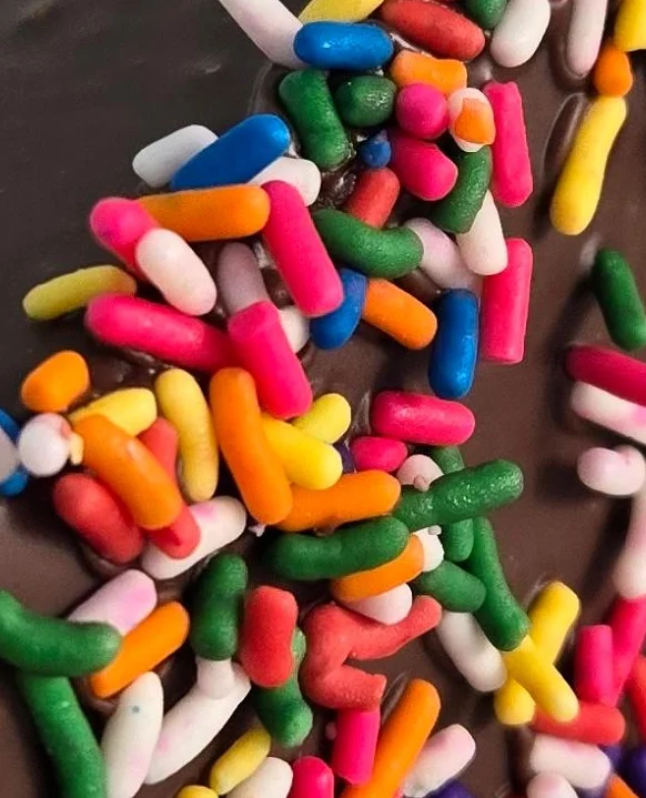 A chocolate-dipped treat covered in colorful sprinkles, resting on a white plate.