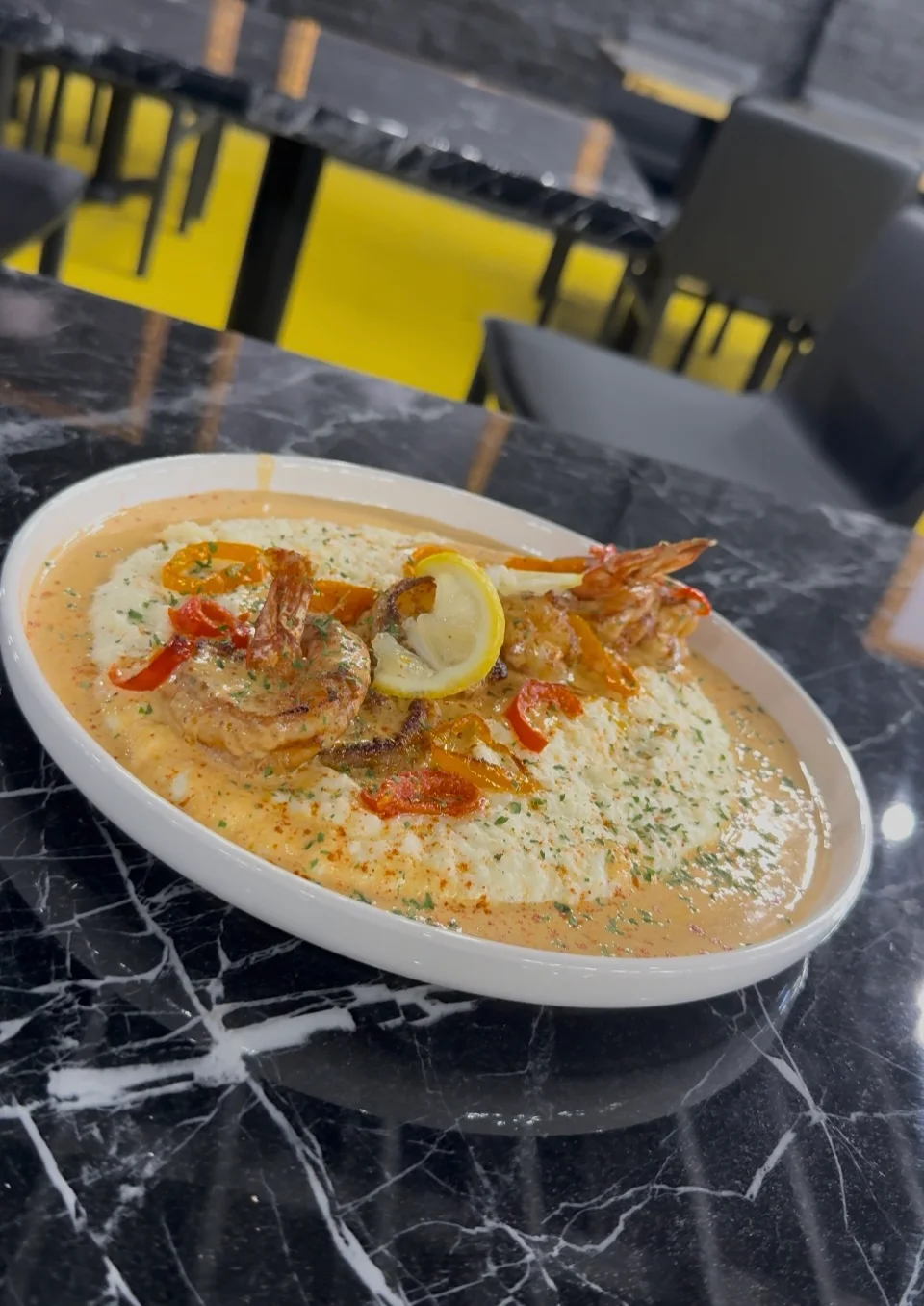 Plate of shrimp with creamy sauce and vegetables on a marble table.