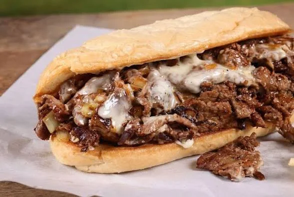 A freshly made sandwich filled with thinly sliced beef, melted cheese, and onions, all inside a soft sub roll.