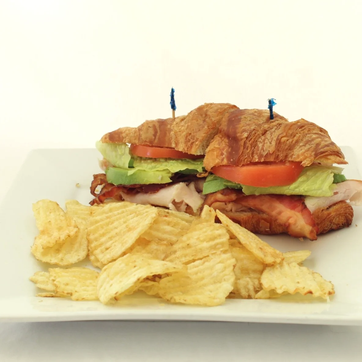 Croissant sandwich with turkey, lettuce, and tomato served with potato chips