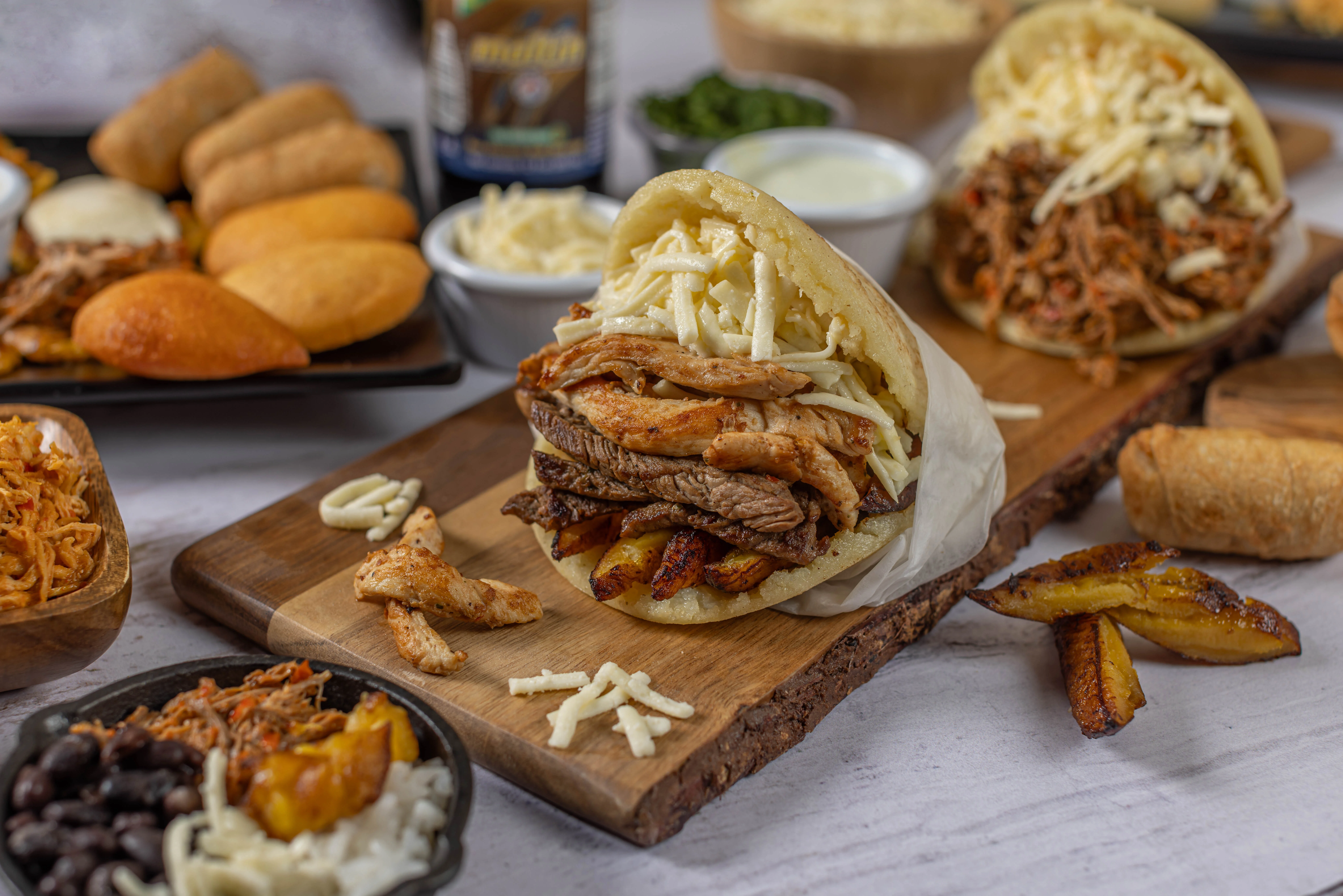 A vibrant feast of authentic Venezuelan and Colombian food, featuring a centerpiece arepa stuffed with chicken and steak, surrounded by empanadas and tequeños.