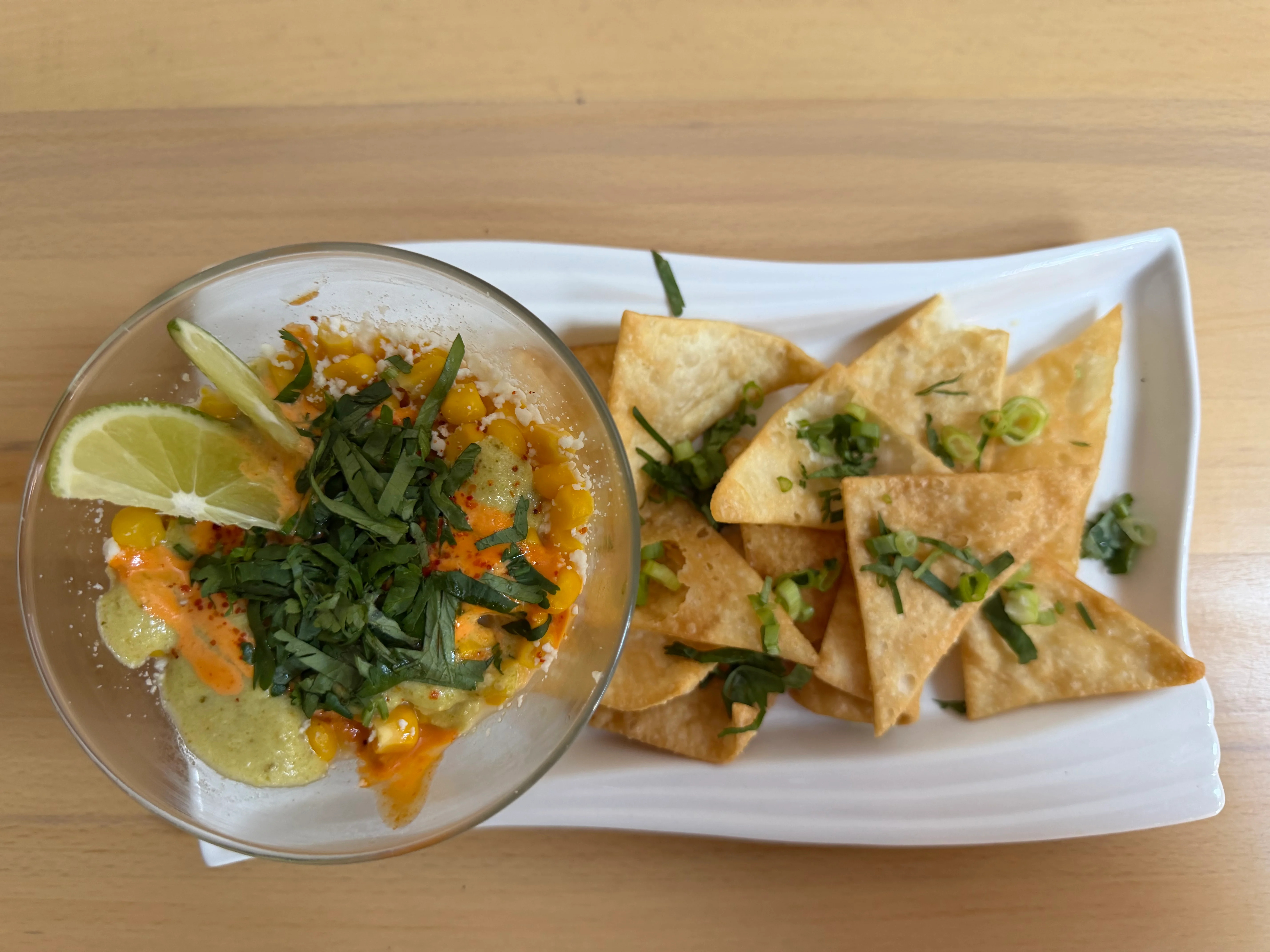 A bowl of corn salad topped with lime, cheese, and herbs, served with crispy tortilla chips.