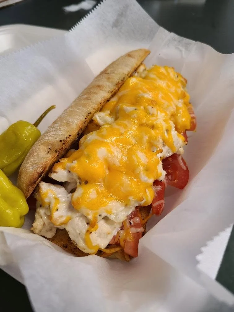 A sandwich filled with chopped chicken, fresh tomatoes, and melted cheese, served with a side of green peppers.