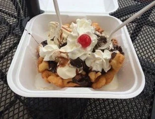 Decadent funnel cake topped with whipped cream and cherry