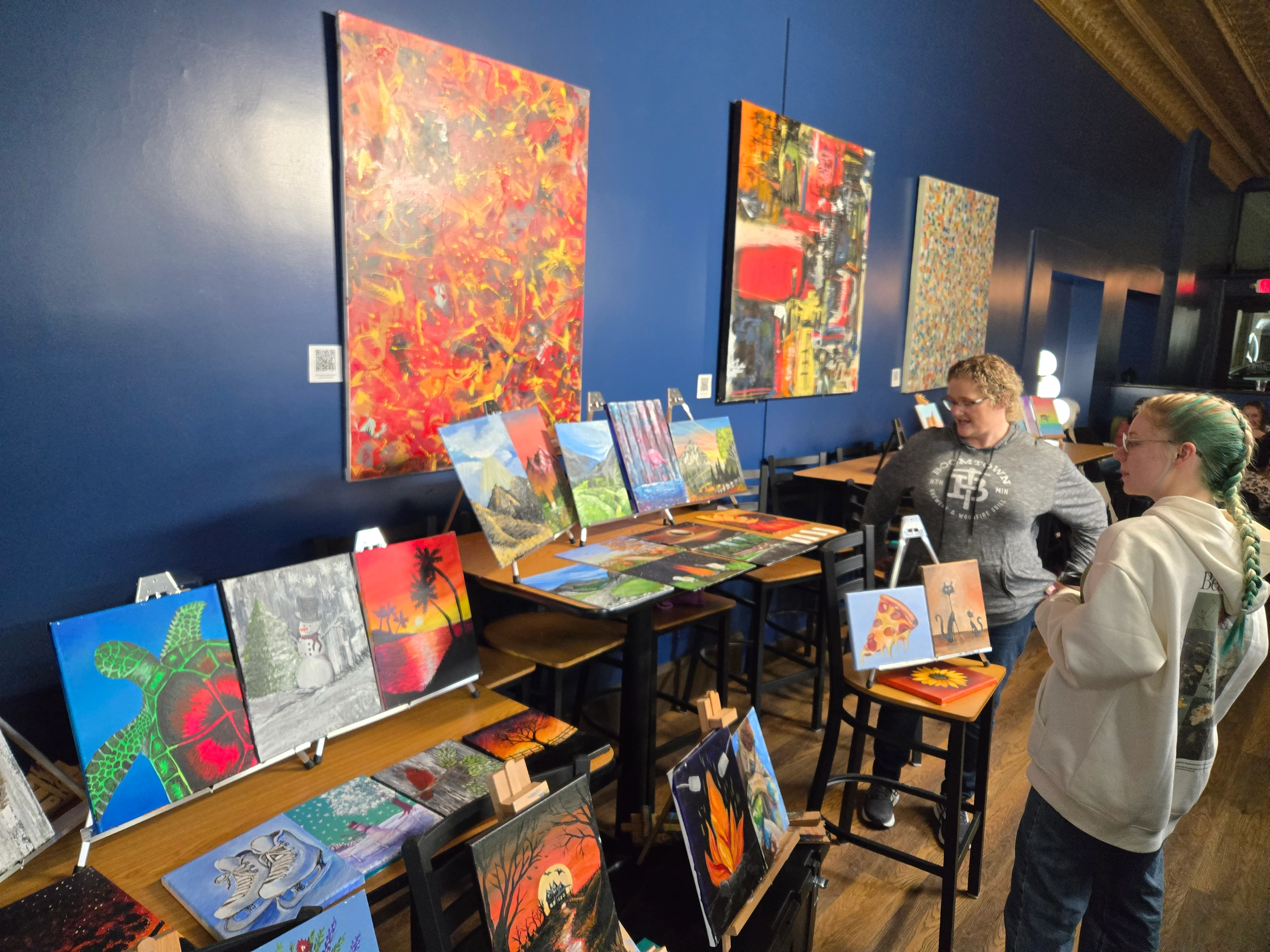 Art display featuring colorful paintings in a cozy cafe setting