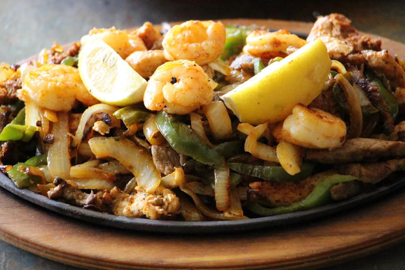 Sizzling shrimp and chicken fajitas with lemon on a wooden platter.