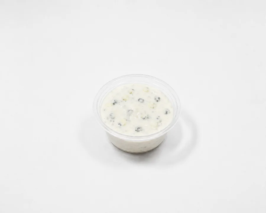 A small container of a creamy, speckled sauce, possibly containing herbs or spices.