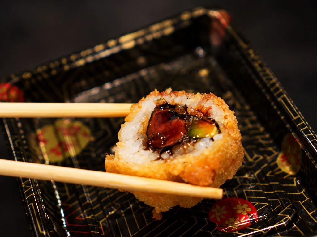 Crispy Japanese sushi roll held with chopsticks