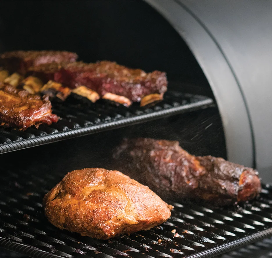 Meat being smoked in a barbecue smoker with a spray bottle.