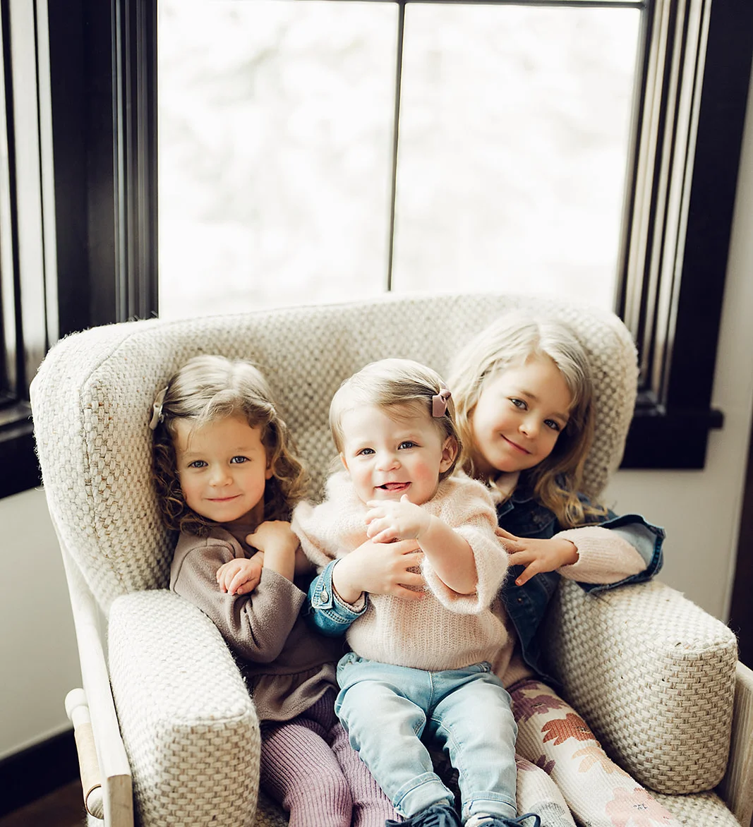Three children smiling together on a cozy chair