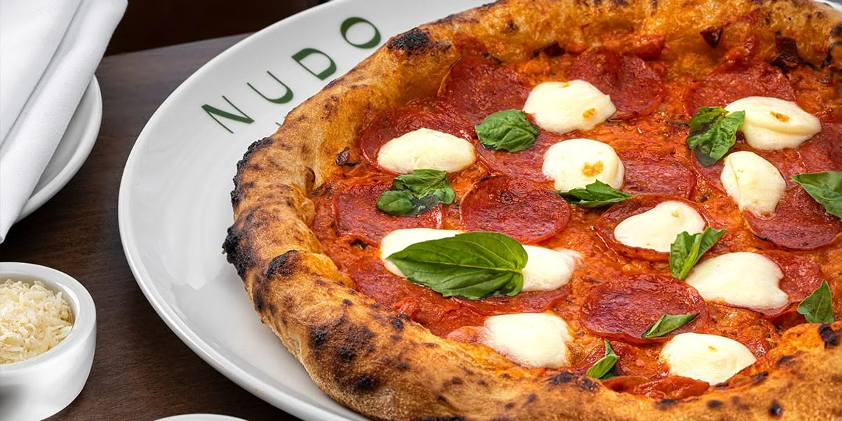 A pepperoni pizza with basil on a plate accompanied by a bowl of freshly grated parmesan cheese. Photo credit: Chris Wessling