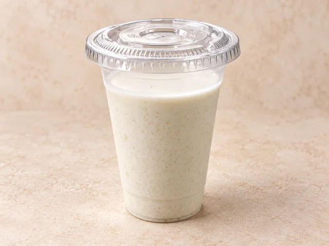 A clear plastic cup filled with a creamy beverage. The drink has a smooth texture and is light in color.