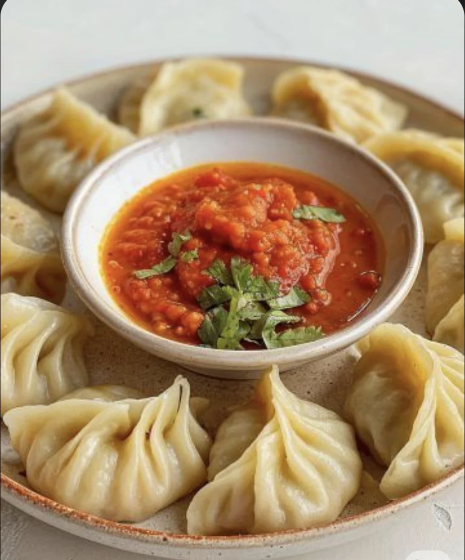 A plate of dumplings arranged around a bowl of spicy dipping sauce, garnished with herbs.