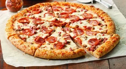 A large pepperoni pizza with a golden crust, topped with slices of pepperoni and cheese. It's placed on a parchment paper over a wooden table.