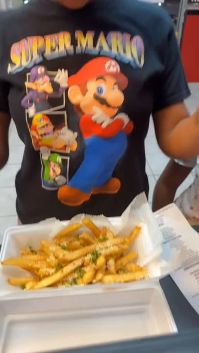 A serving of seasoned French fries topped with grated cheese and herbs, presented in a white takeout container.