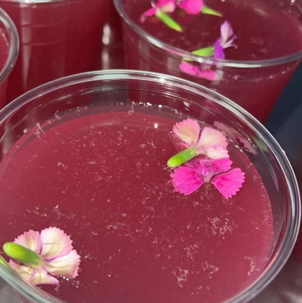 A close-up of vibrant pink beverages in clear cups, each garnished with delicate edible flowers.