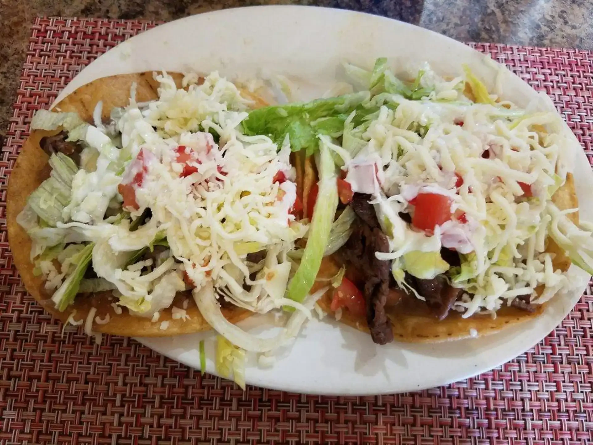 Two crispy tostadas from El Ranchito Poblano, generously topped with steak, shredded lettuce, cheese, and cream.