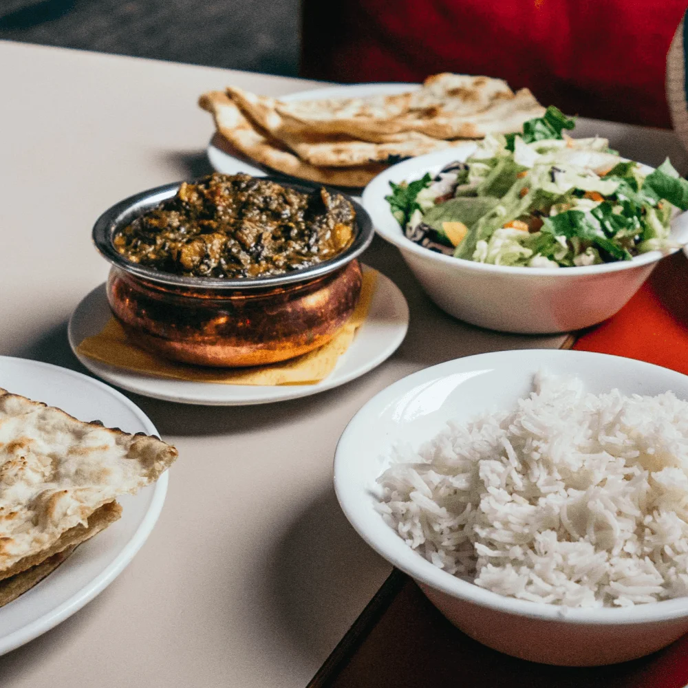 Indian meal with white rice, a bowl of brown curry, salad, and naan bread.
