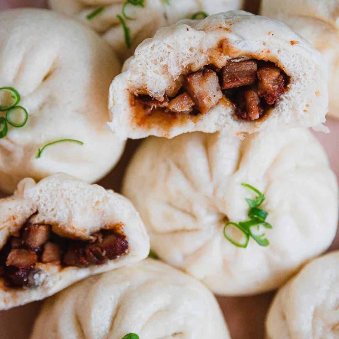Steamed buns filled with savory meat, garnished with green onions.