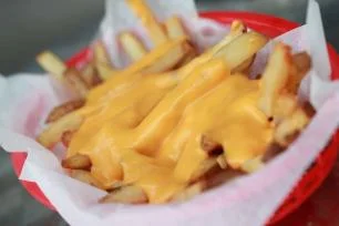 A sandwich filled with shredded meat, accompanied by a side of crispy French fries. The sandwich is served in a paper-lined basket.