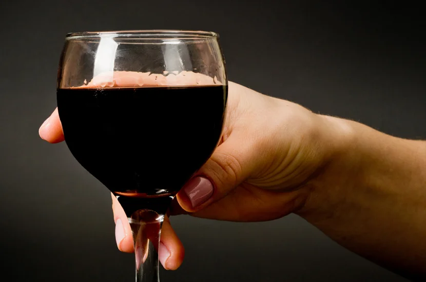 Hand holding a glass of red wine against a dark background